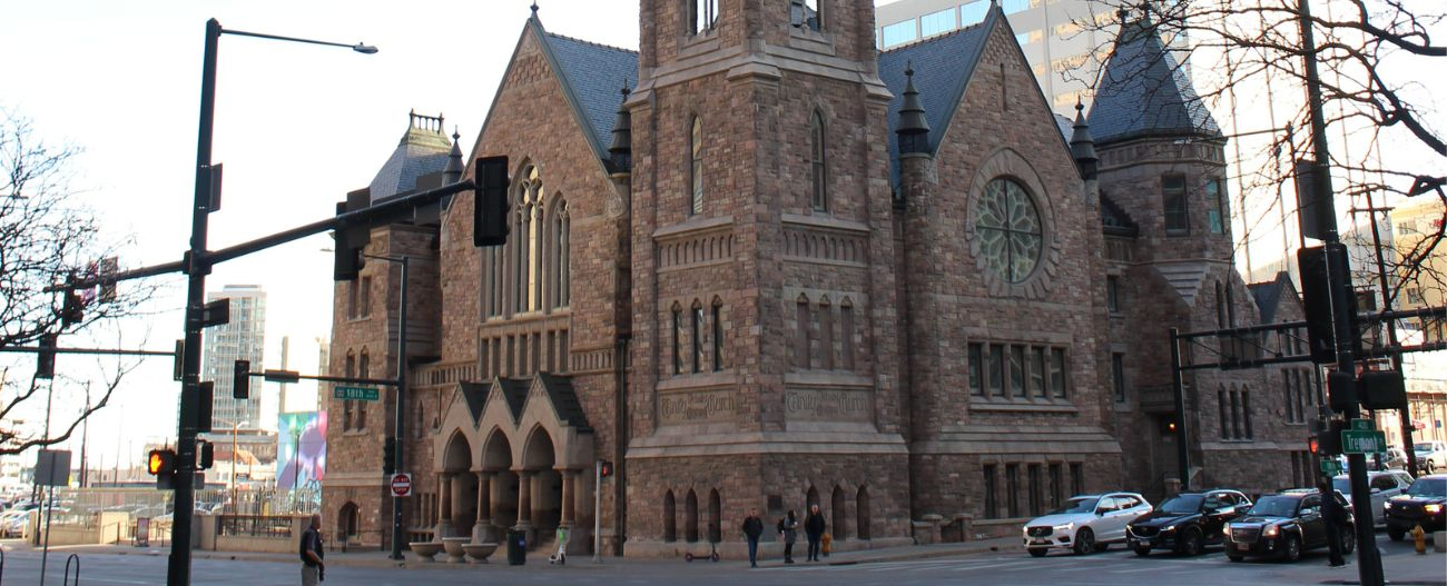 Image of a Victorian-style brick building in the corner of an intersection with cars and pedestrians present