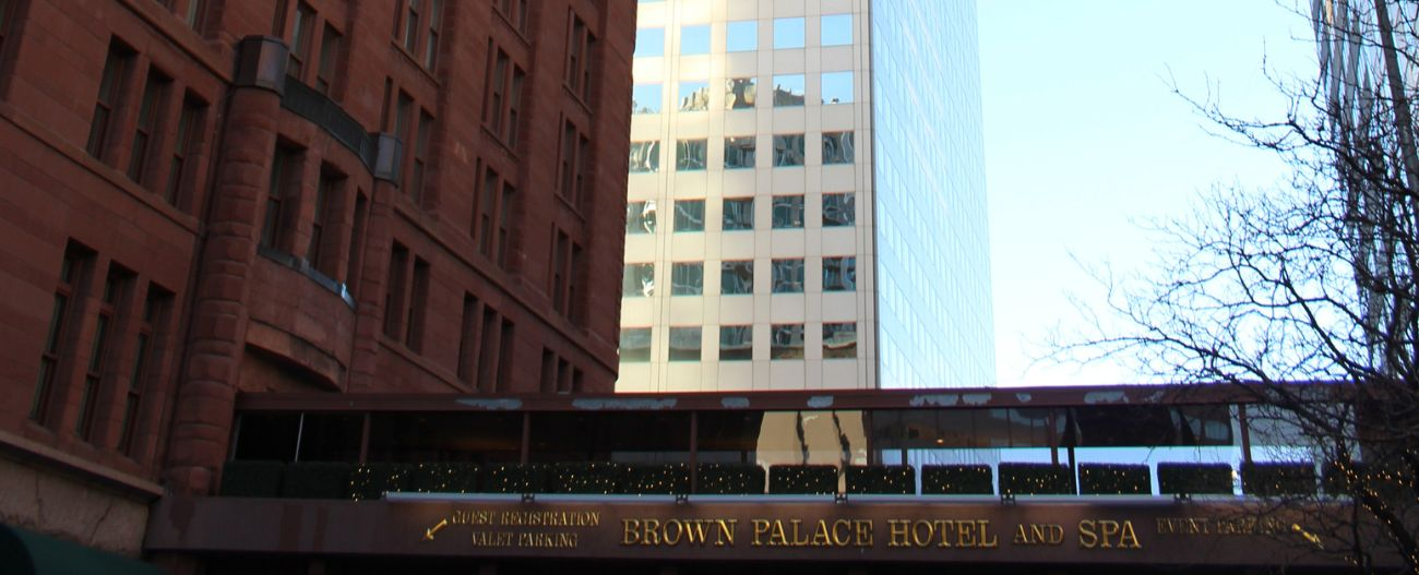 Image of a red brick building with an overpass featuring gold lettering against a background consisting of a tall skyscraper building and light blue sky
